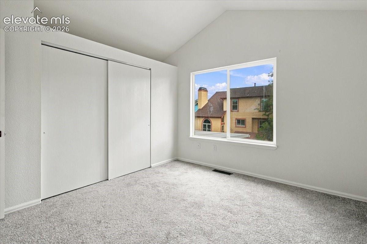 Interior space featuring vaulted ceilings, neutral wall tones, wall-to-wall carpeting, and a double-door sliding closet
