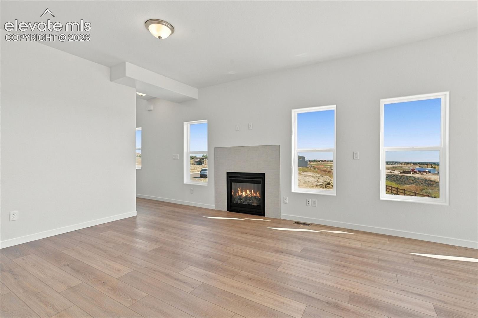Wood-finish flooring, white walls, recessed ceiling light, fireplace with a tiled surround, and multiple windows