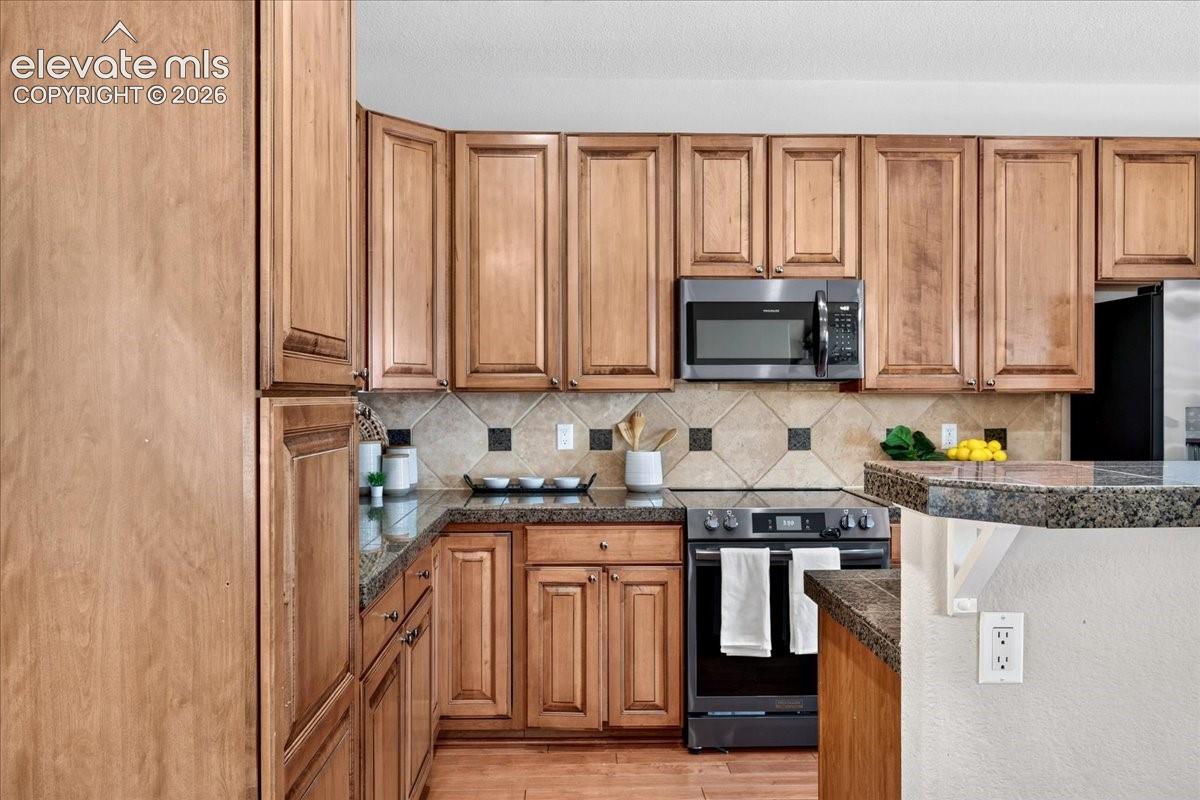 Wood-finish cabinetry, granite-style countertops, tile backsplash with accent inserts, stainless steel microwave, and a black electric range