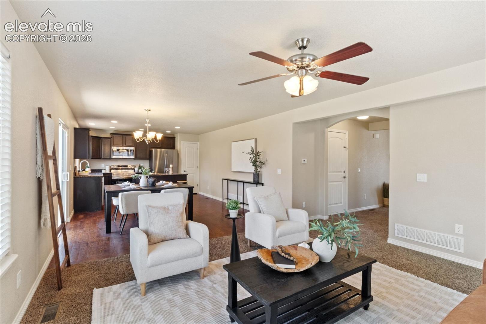 Open-concept living space featuring a ceiling fan, carpet flooring, and an arched doorway