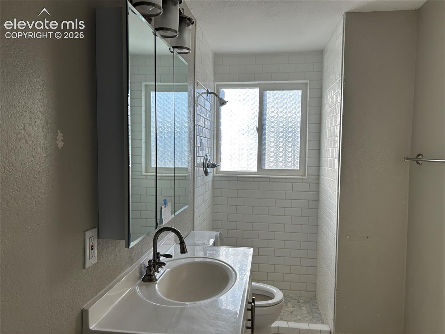 Bathroom featuring a vanity with a white countertop and oval basin, integrated mirrored medicine cabinet, subway tile shower surround, and sliding window with obscured glass