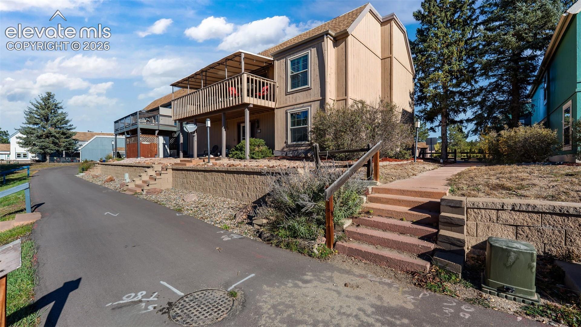 Multi-level wood siding exterior featuring a second-story wooden deck, concrete retaining wall, and tiered stone staircases