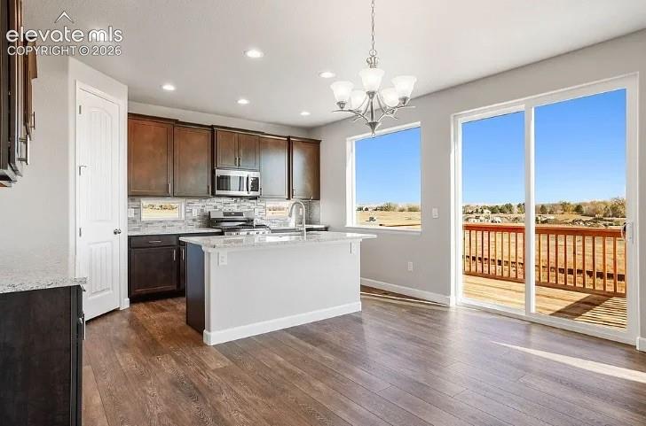 Kitchen featuring dark-toned cabinetry, stone-surface countertops, wood-finish flooring, a multi-light chandelier, and sliding glass doors leading to an exterior deck