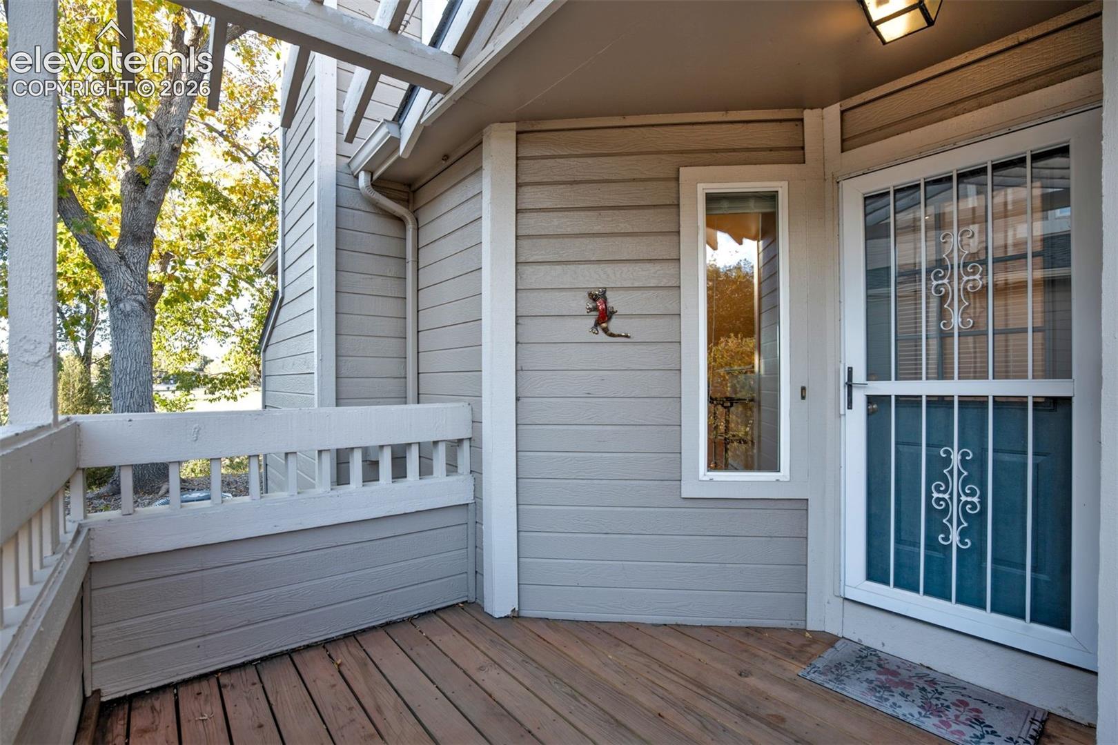 Covered exterior deck featuring wood-finish decking, horizontal lap siding, a protective metal screen door, and a built-in overhead pergola structure