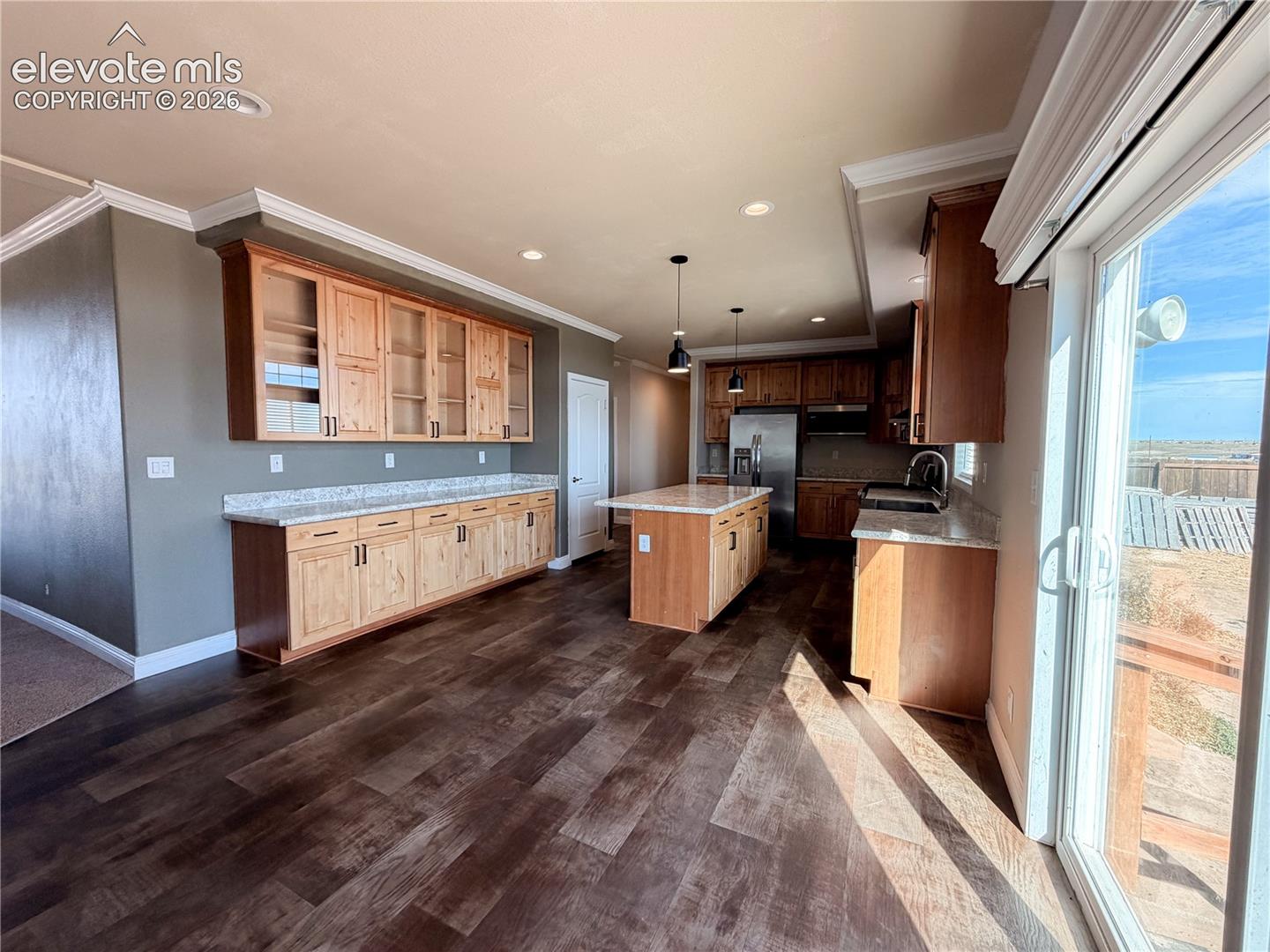 Kitchen featuring wood-finish cabinetry, an island with stone-style countertops, recessed lighting, and sliding glass doors