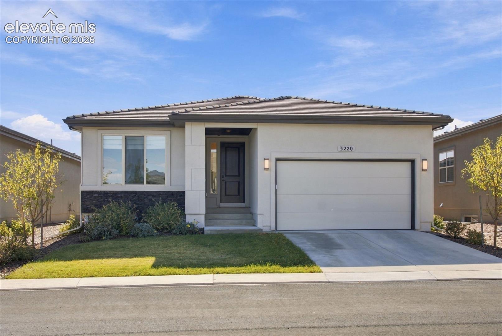 Single-story residence featuring a smooth stucco facade with stone veneer accents, a low-pitch hipped roof, a two-car garage, and a concrete driveway