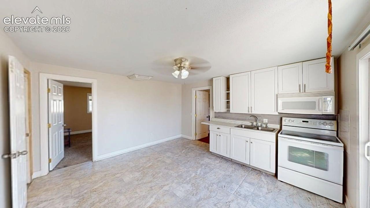 White cabinetry, white appliances, light-toned flooring, and a ceiling fan