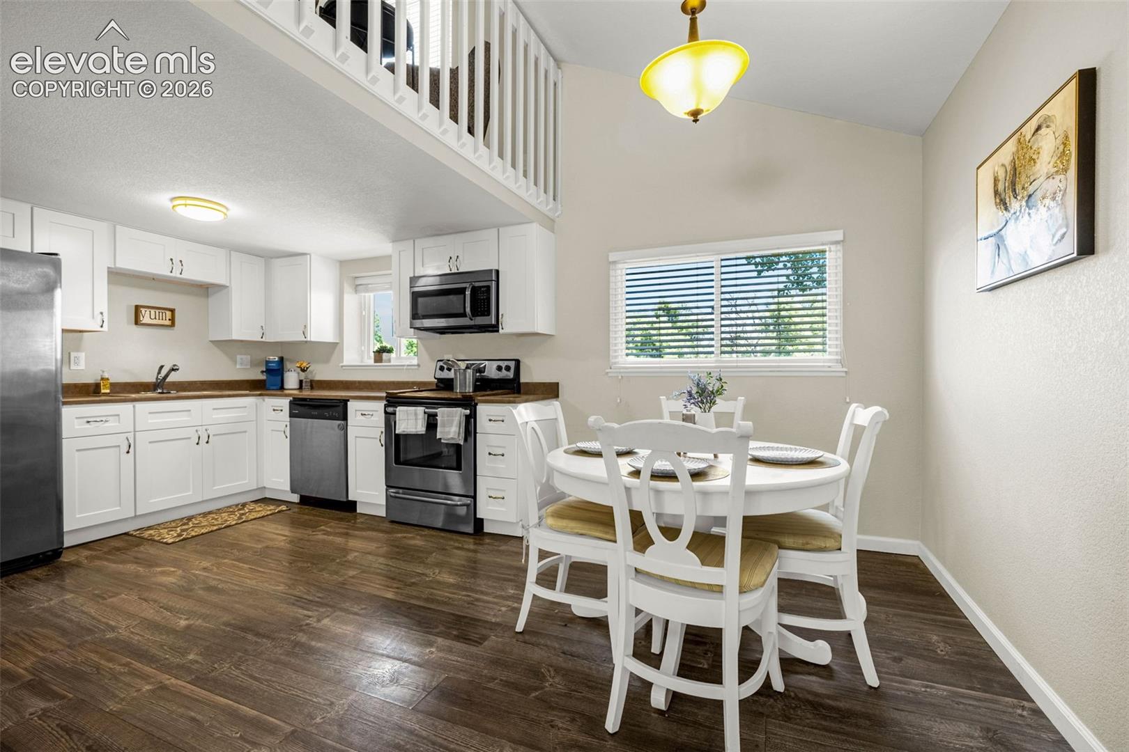 Kitchen featuring white cabinetry, wood-finish flooring, stainless steel appliances, vaulted ceilings, and a mezzanine balcony with white balusters
