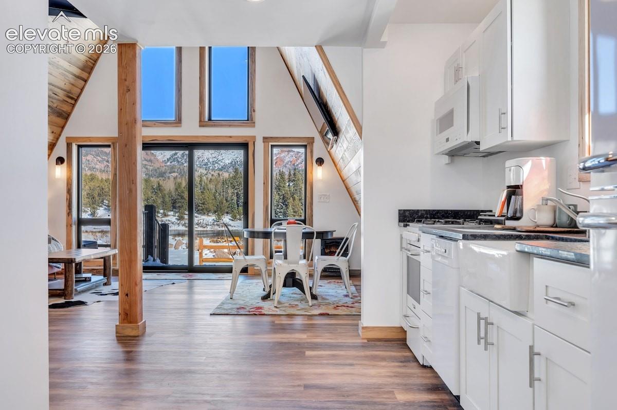 A-frame architectural design with wood-finish flooring, white shaker-style cabinetry, apron-front farmhouse sink, and expansive floor-to-ceiling windows