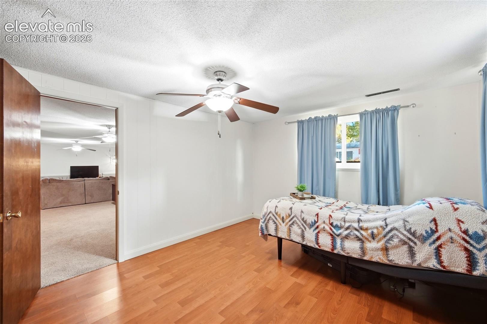 Wood-finish flooring, ceiling fan with integrated lighting, and window with metal curtain hardware