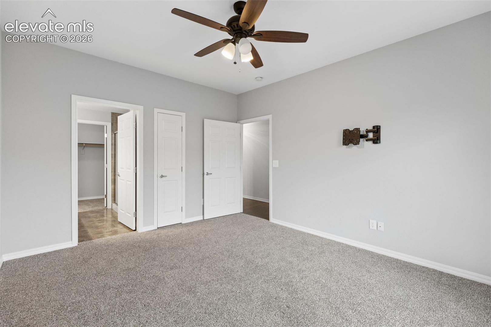 Room featuring wall-to-wall carpeting, a multi-blade ceiling fan with integrated light fixture, and multiple paneled interior doors