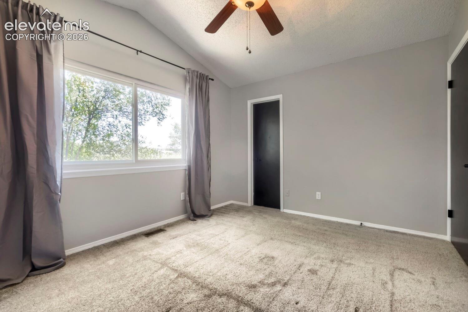 Vaulted ceiling room with ceiling fan light fixture, gray carpet flooring, and neutral wall paint