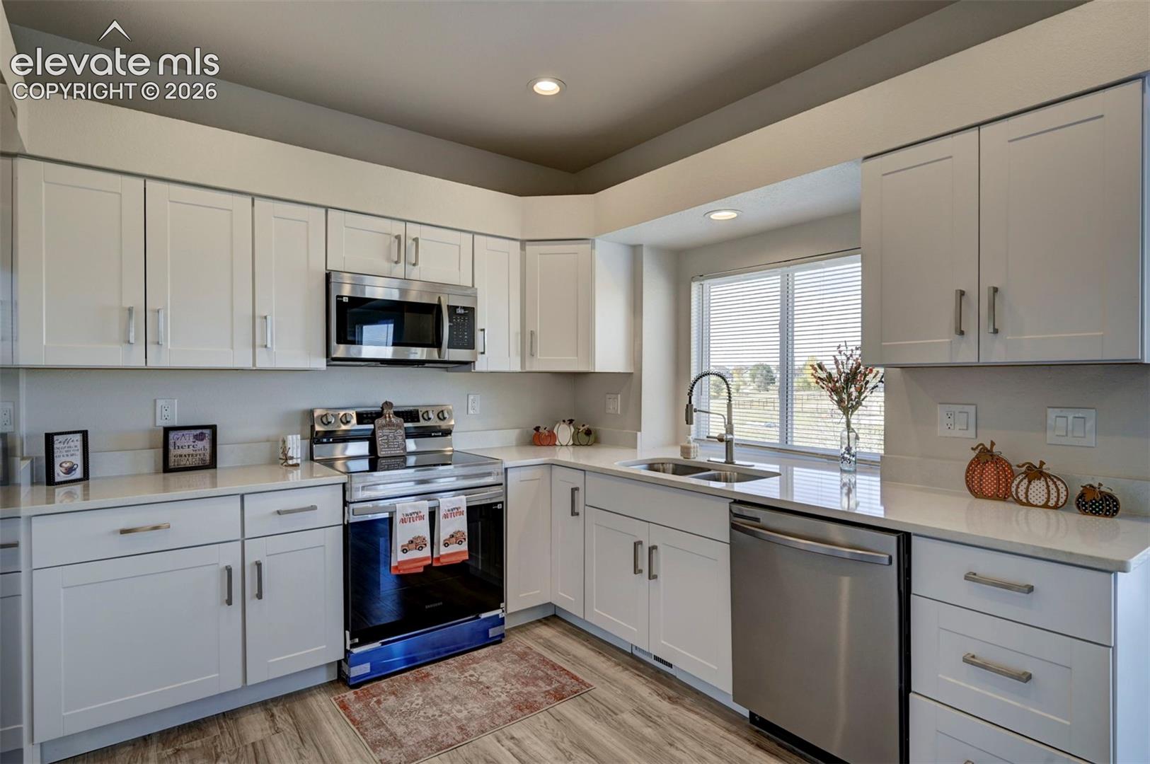 Kitchen featuring white shaker-style cabinetry, solid-surface countertops, stainless steel appliances, a pull-down kitchen faucet, and wood-finish flooring
