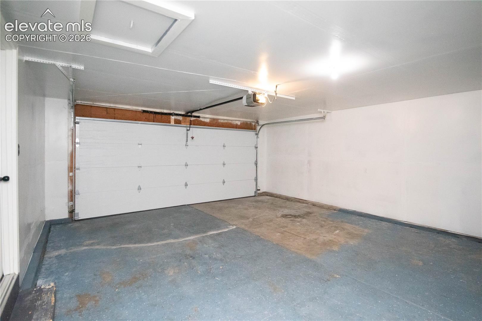 Attached garage featuring a white paneled overhead door, automatic door opener, finished ceiling with an access hatch, and painted walls