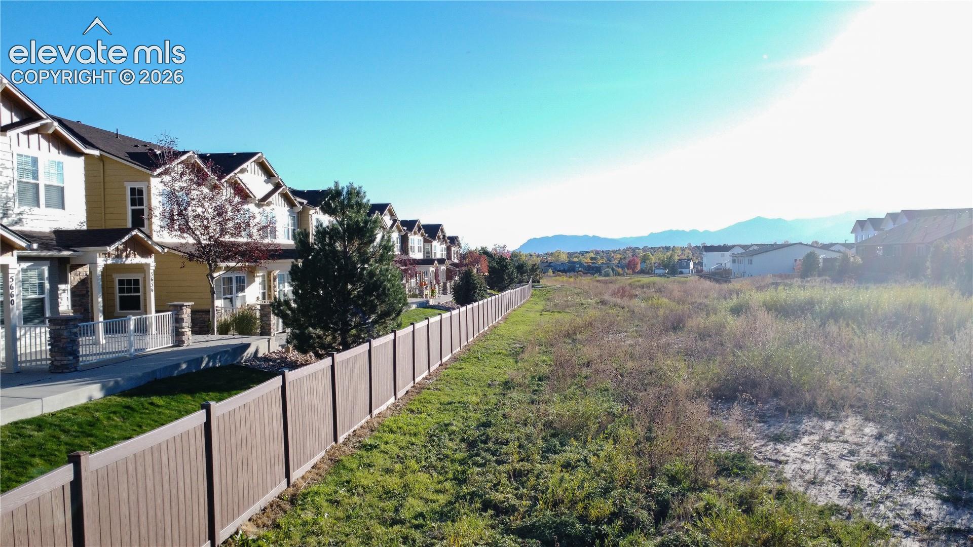 Multi-story townhomes featuring stone and siding facades, concrete walkways, solid-panel privacy fencing, and a natural landscape backdrop with mountain silhouettes