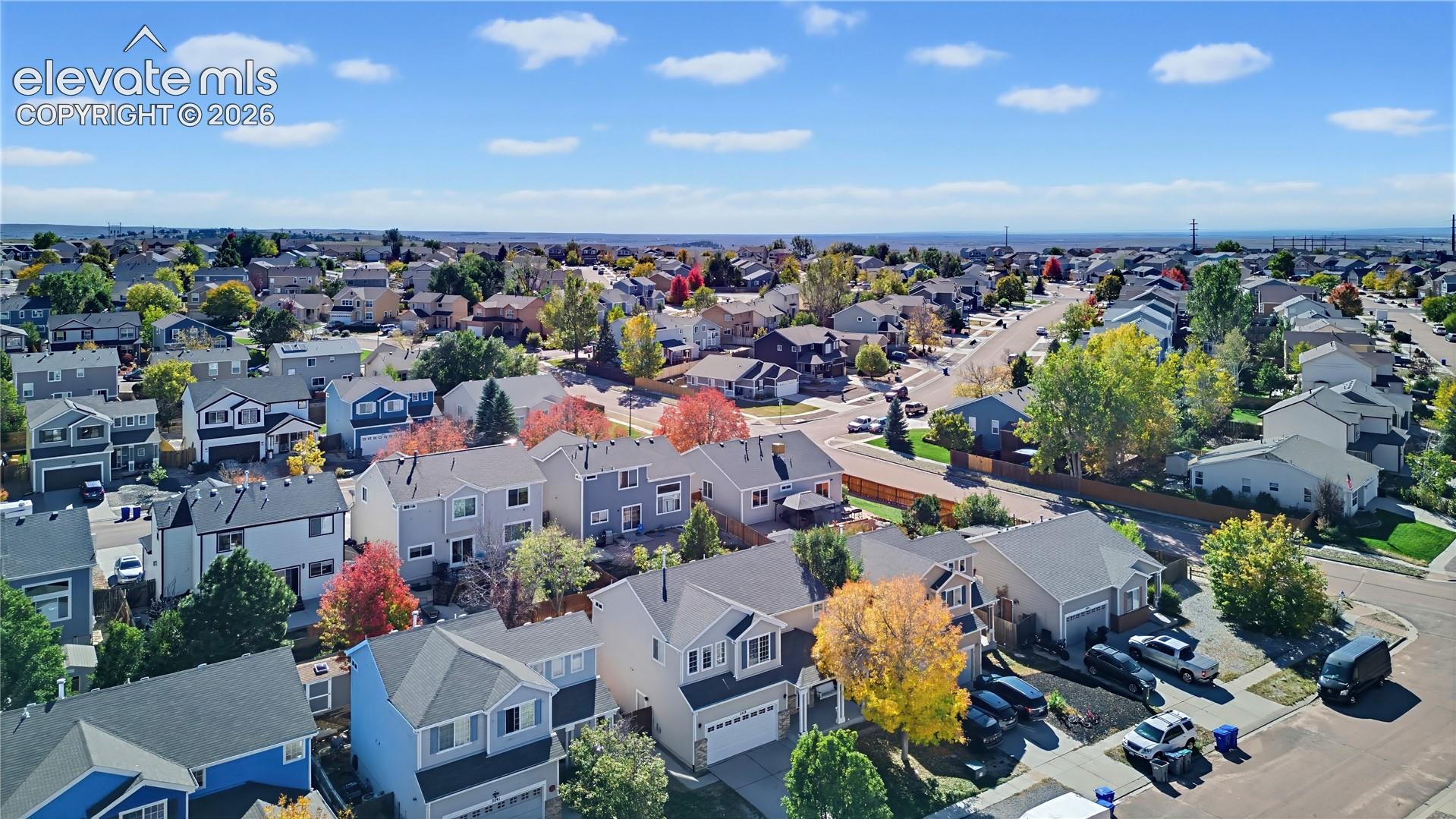 Aerial perspective of a suburban neighborhood featuring multi-level residential structures, paved street networks, mature deciduous trees, and expansive horizon surroundings