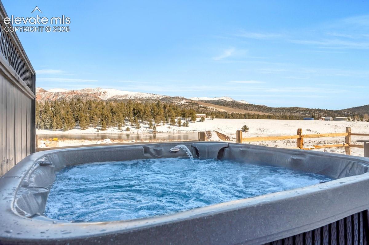Outdoor spa with built-in water feature, wood-slat privacy screen, and timber-post fencing set against a mountain and water backdrop
