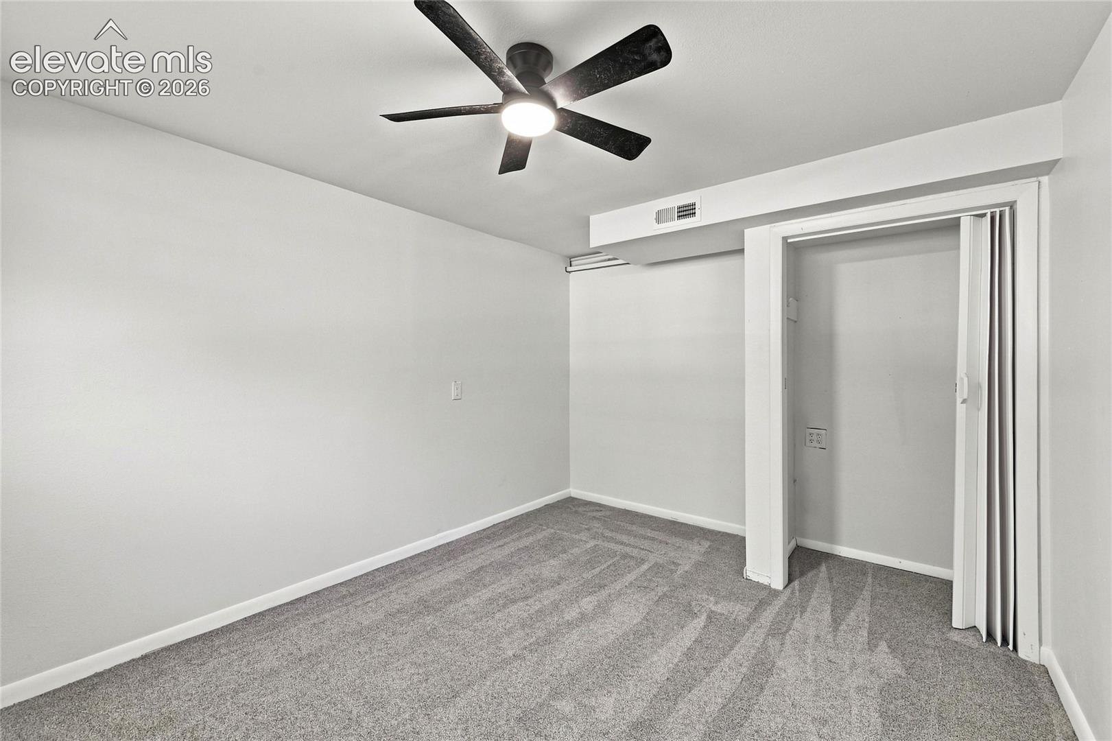 Ceiling fan with integrated lighting, neutral wall paint, gray patterned carpeting, and bi-fold closet doors
