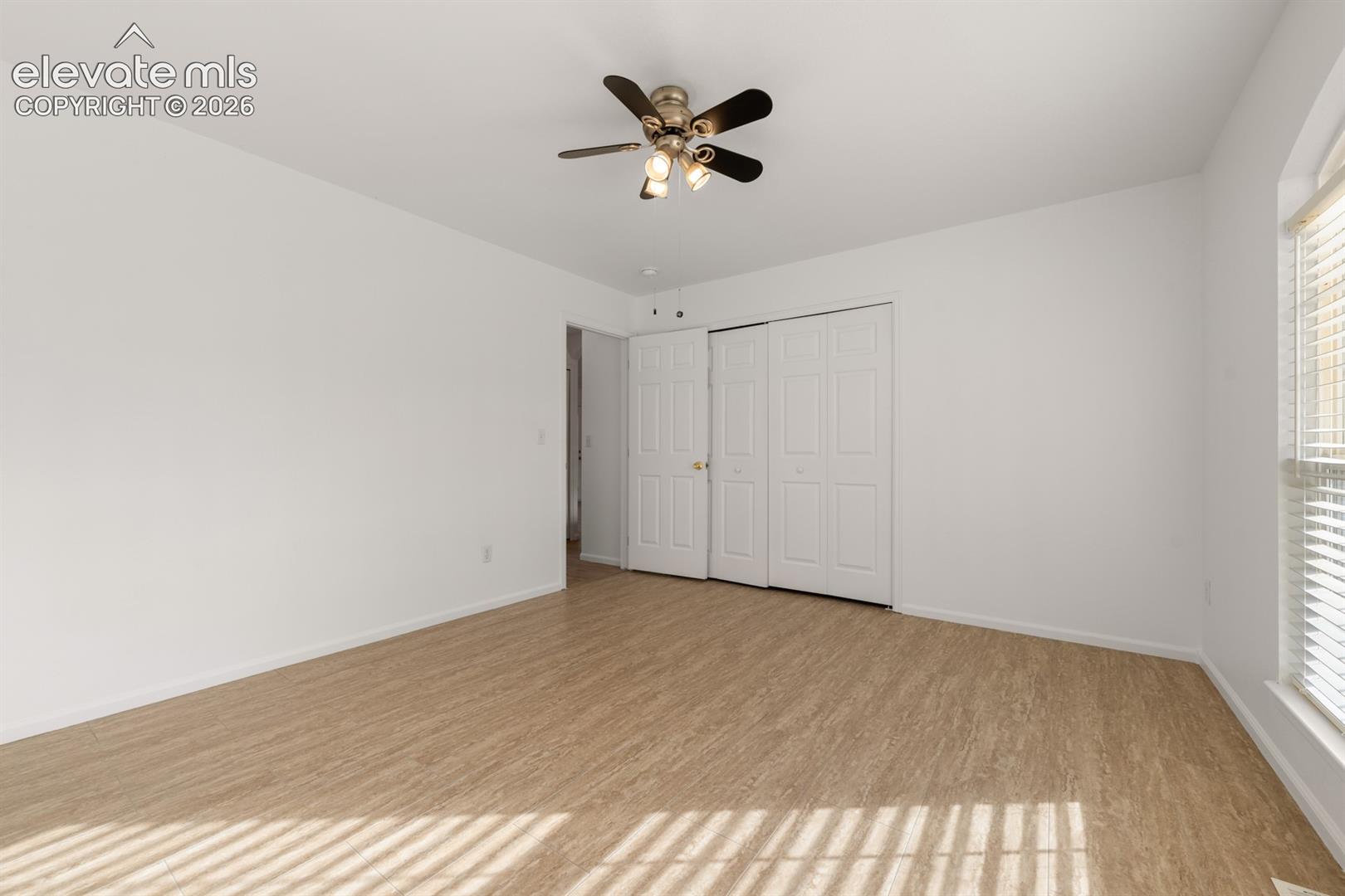 Neutral-toned interior featuring wood-finish flooring, a multi-blade ceiling fan with integrated lighting, and a multi-panel closet door