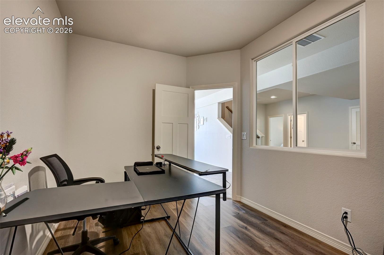 Dedicated room with wood-finish flooring, light-toned wall paint, white trim, and an interior window providing visibility to an additional area