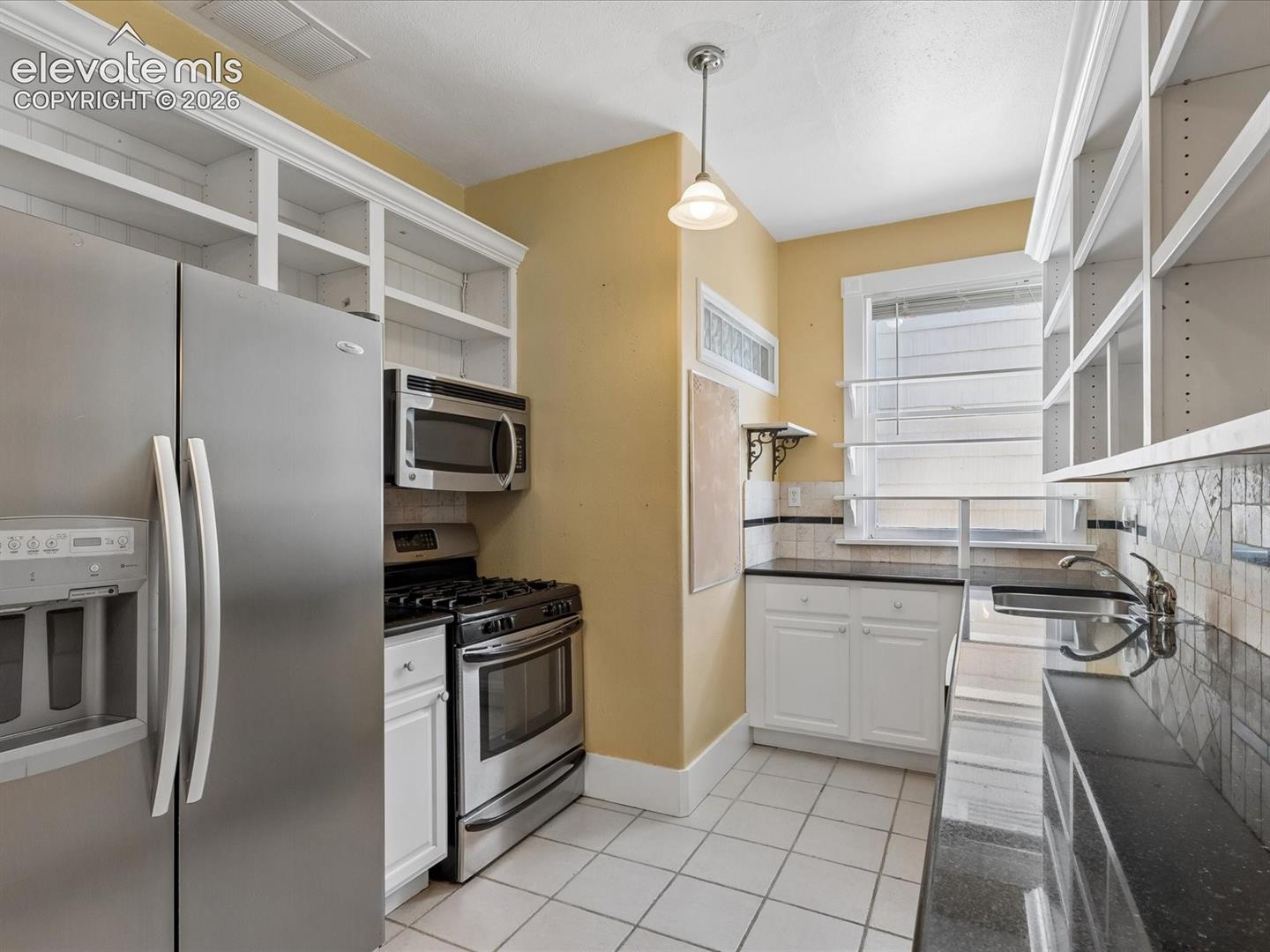 Galley kitchen featuring white cabinetry, stainless steel appliances, black countertops, and a decorative tile backsplash