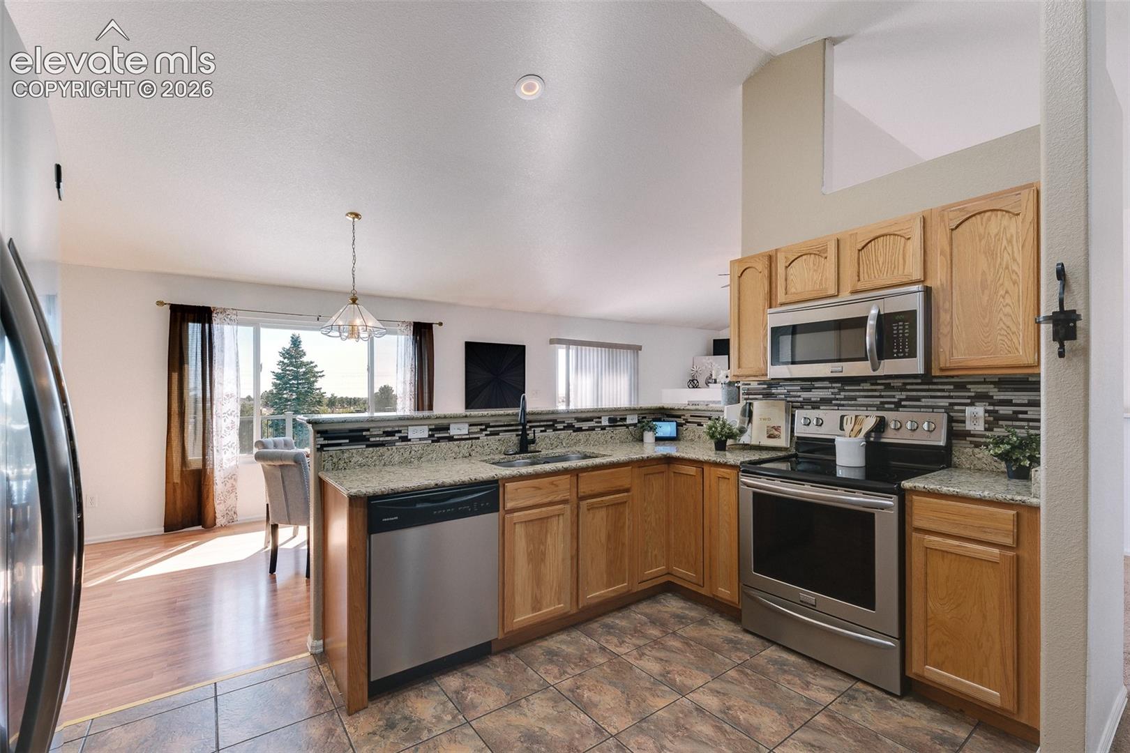 Beautiful kitchen showcasing granite countertops, stainless steel appliances, oak cabinetry, tile flooring, and a convenient breakfast bar overlooking the main living space.