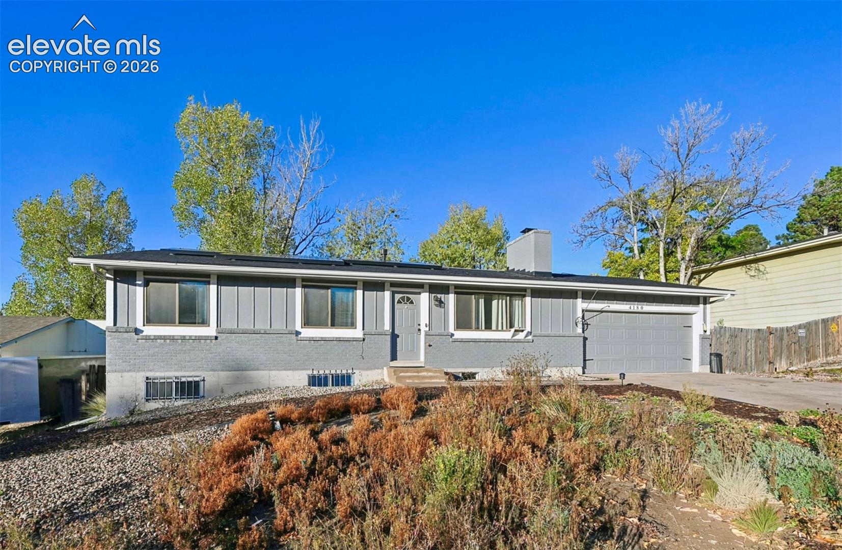 Single-story exterior featuring a brick and vertical siding facade, attached two-car garage, and a low-profile roofline with solar panels for energy efficiency! 