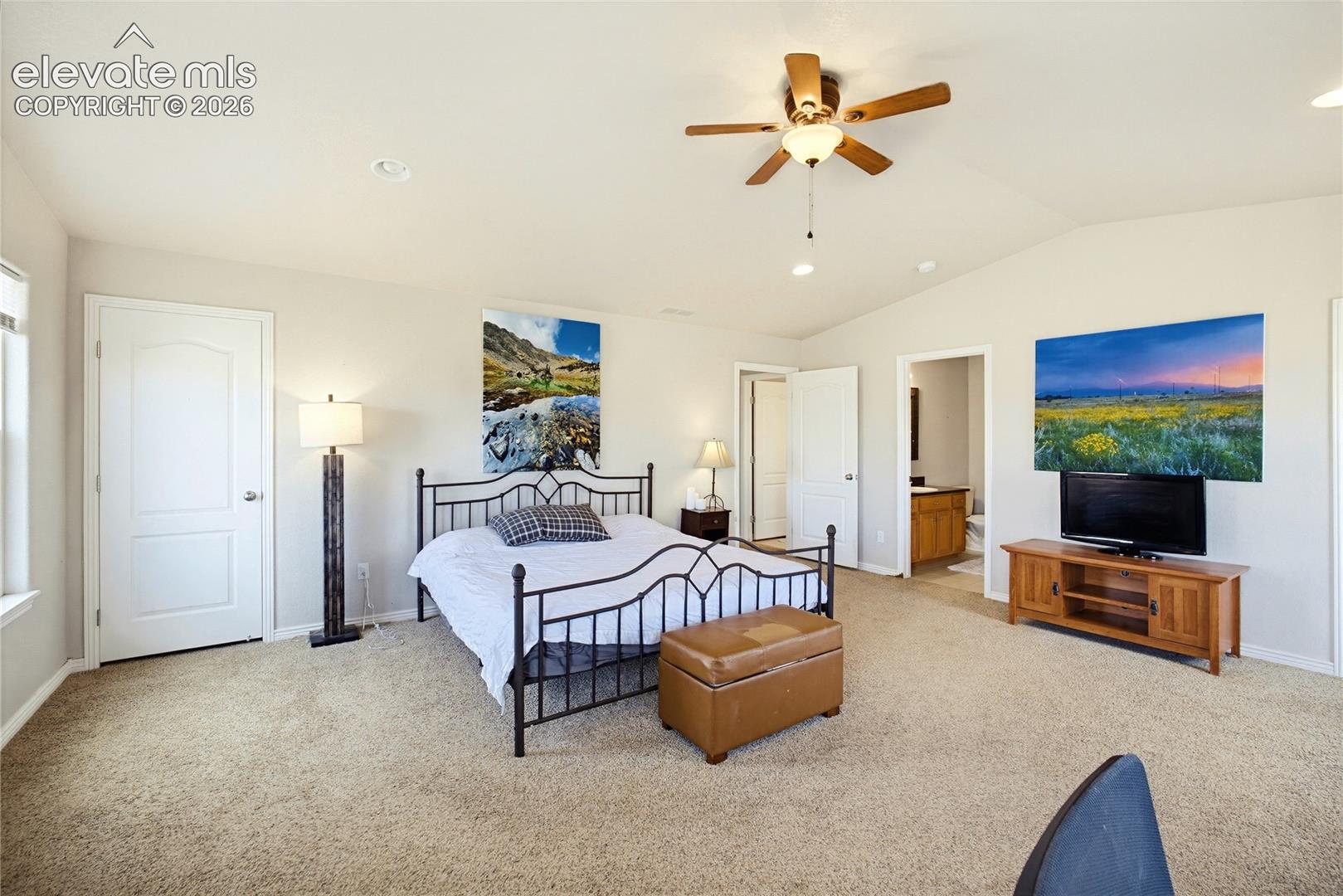 Spacious bedroom featuring vaulted ceilings, neutral wall tones, wall-to-wall carpeting, and a ceiling fan with integrated lighting