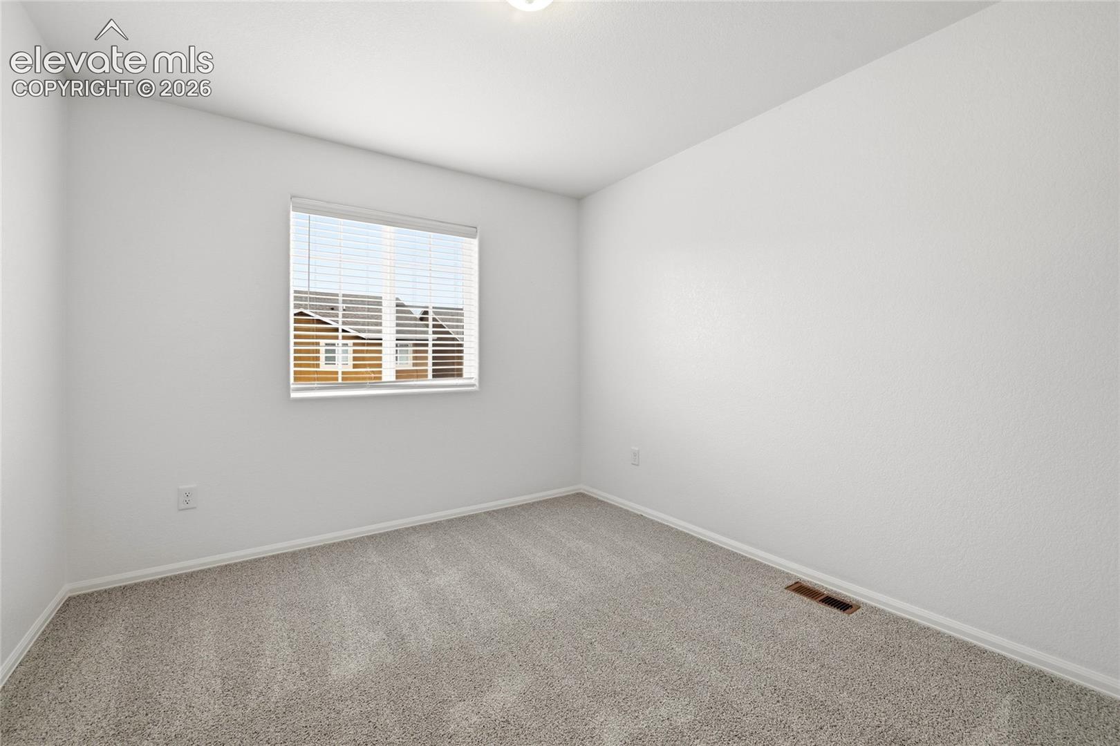 Neutral-toned interior space featuring light-colored wall-to-wall carpeting, crisp white walls, and a single window with horizontal blinds
