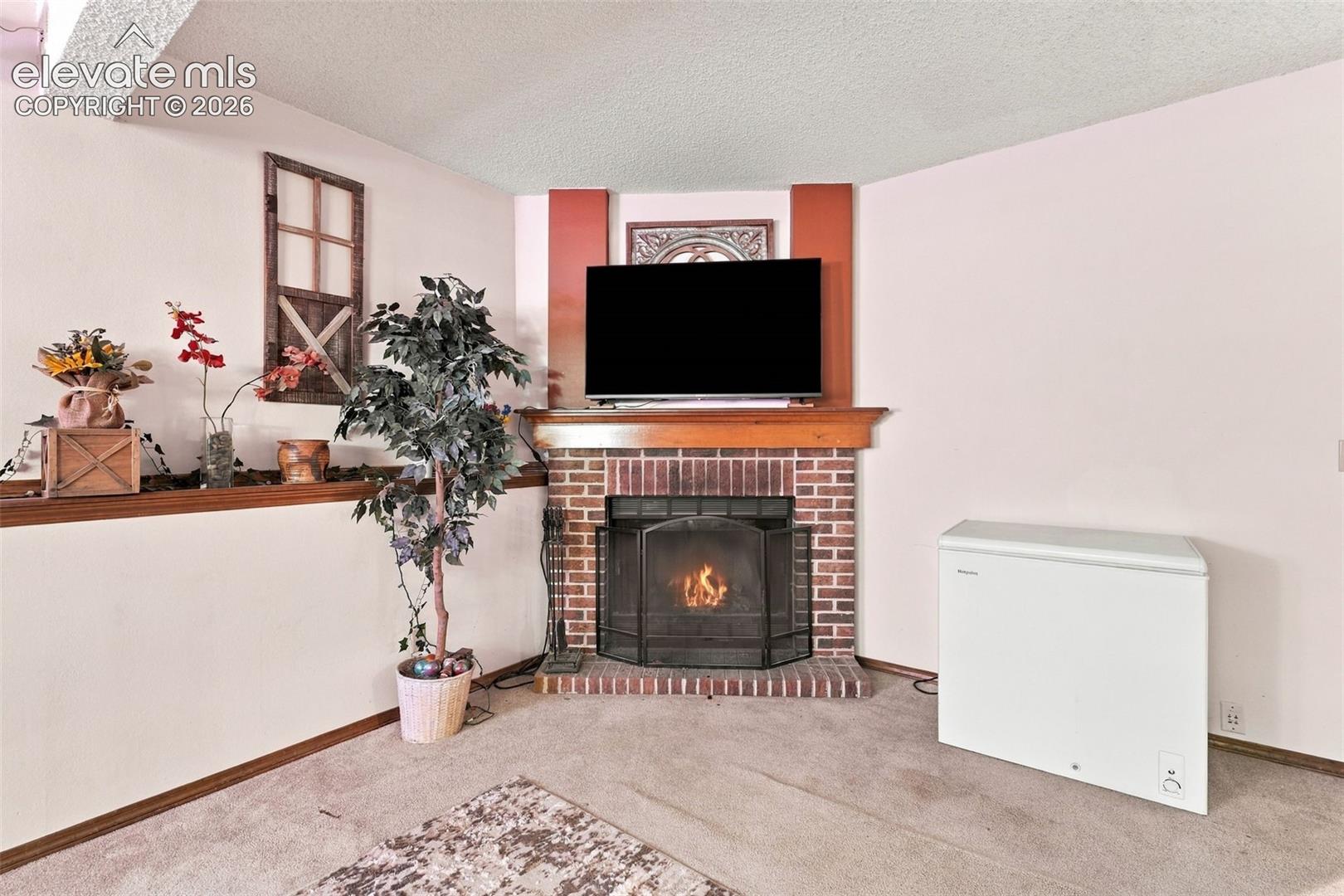 Corner fireplace with a brick surround, elevated brick hearth, and wood mantel, featuring a metal fireplace screen