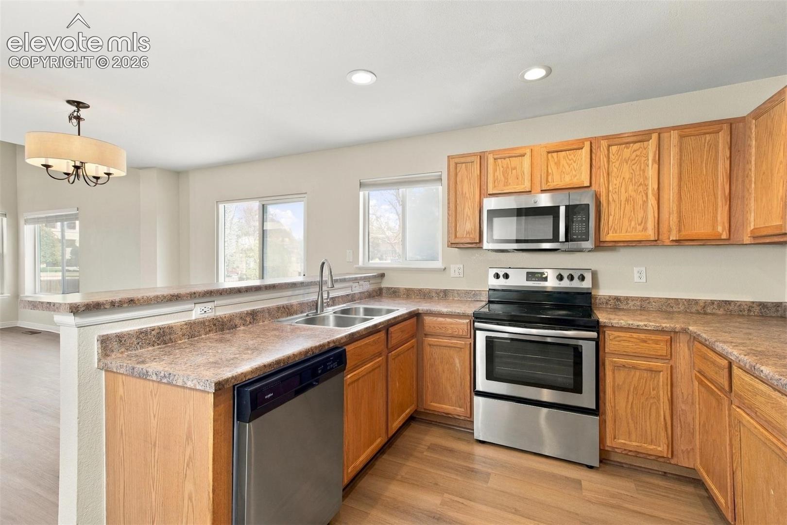 Kitchen featuring wood cabinetry, stainless steel appliances, laminate countertops, a dual-basin sink, and wood-finish flooring