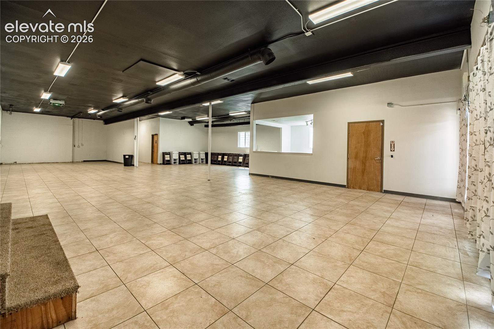 Expansive open space featuring tile flooring, a dark finished ceiling, recessed lighting, and a service window