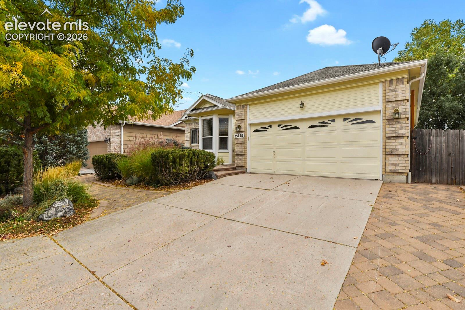 Single-story residence featuring a two-car garage, brick and siding exterior, bay window, concrete driveway, and paver stone walkway