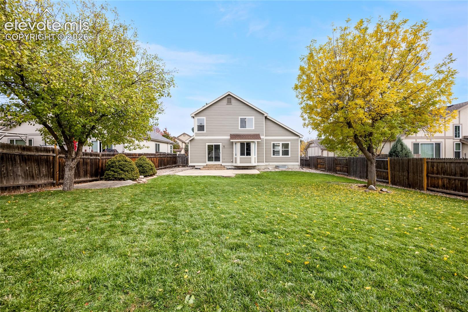 Backyard featuring a grass lawn, paved patio, mature trees, and wood privacy fencing