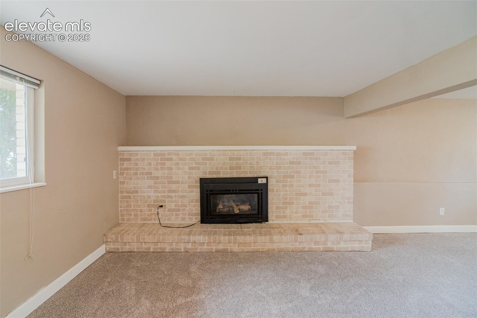 Brick fireplace with a raised hearth, light-colored walls, and carpeting