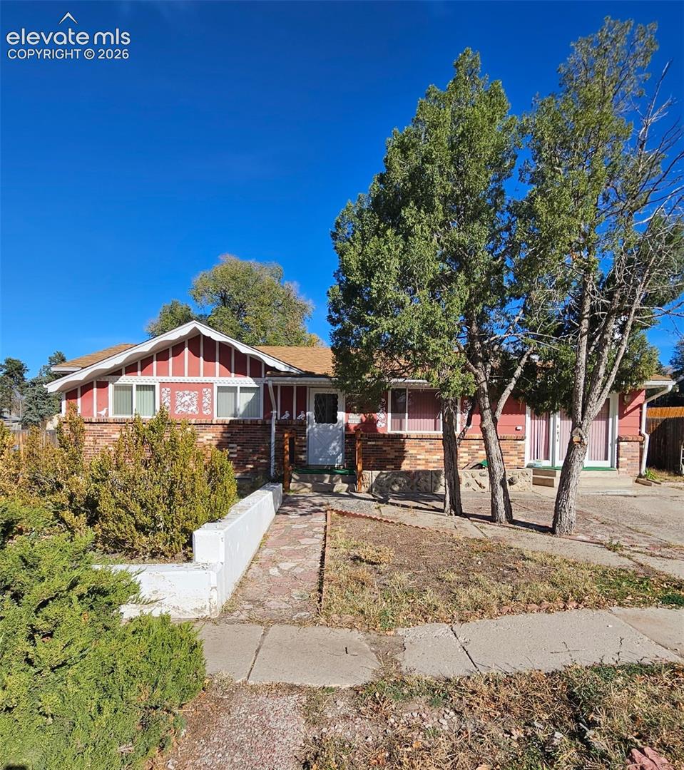 Single-story residence featuring brick and vertical siding exterior, decorative gable detailing, concrete walkway, and mature landscaping