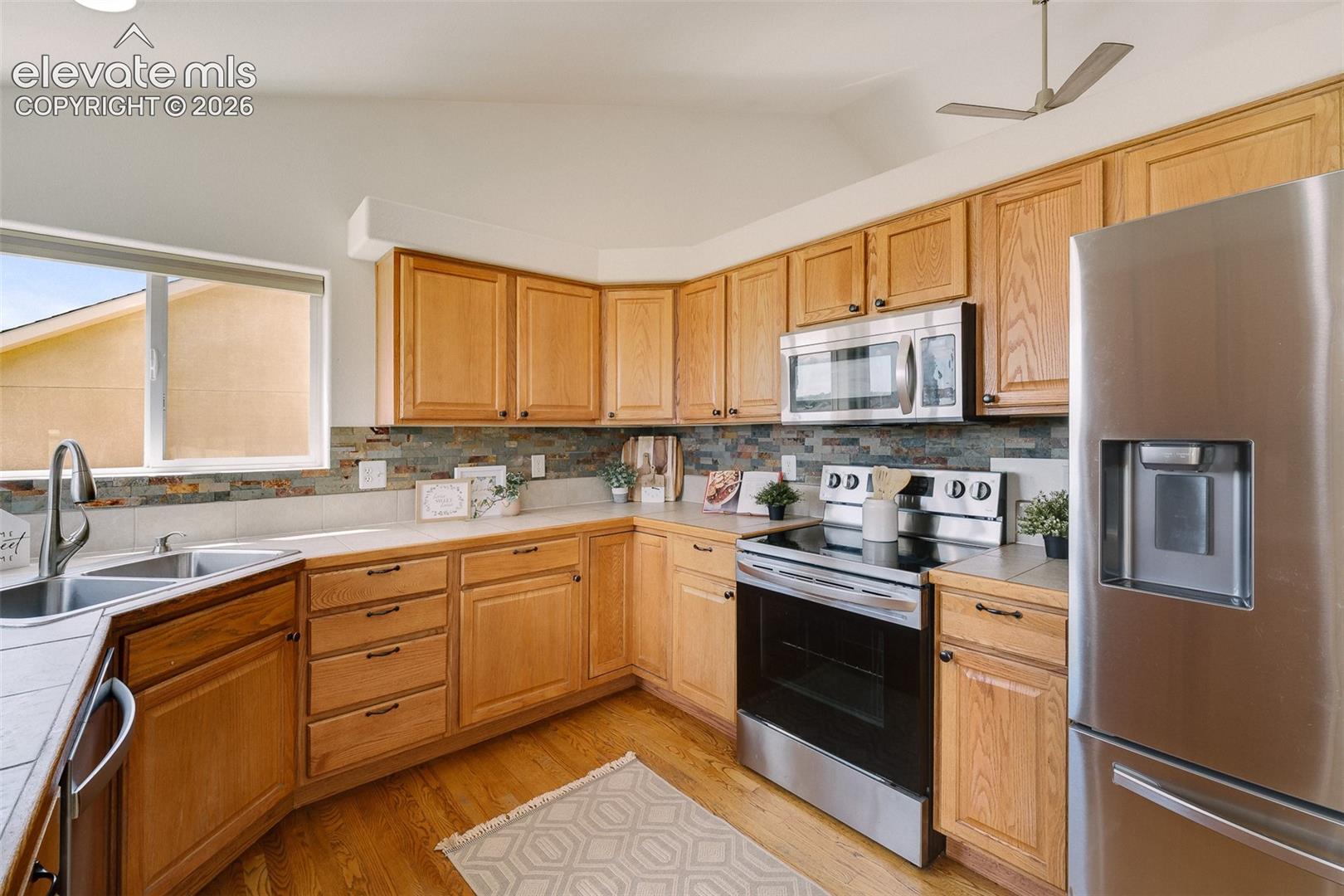 Kitchen featuring wood-finish cabinetry, stainless steel appliances, a multi-tone backsplash, and a double basin sink