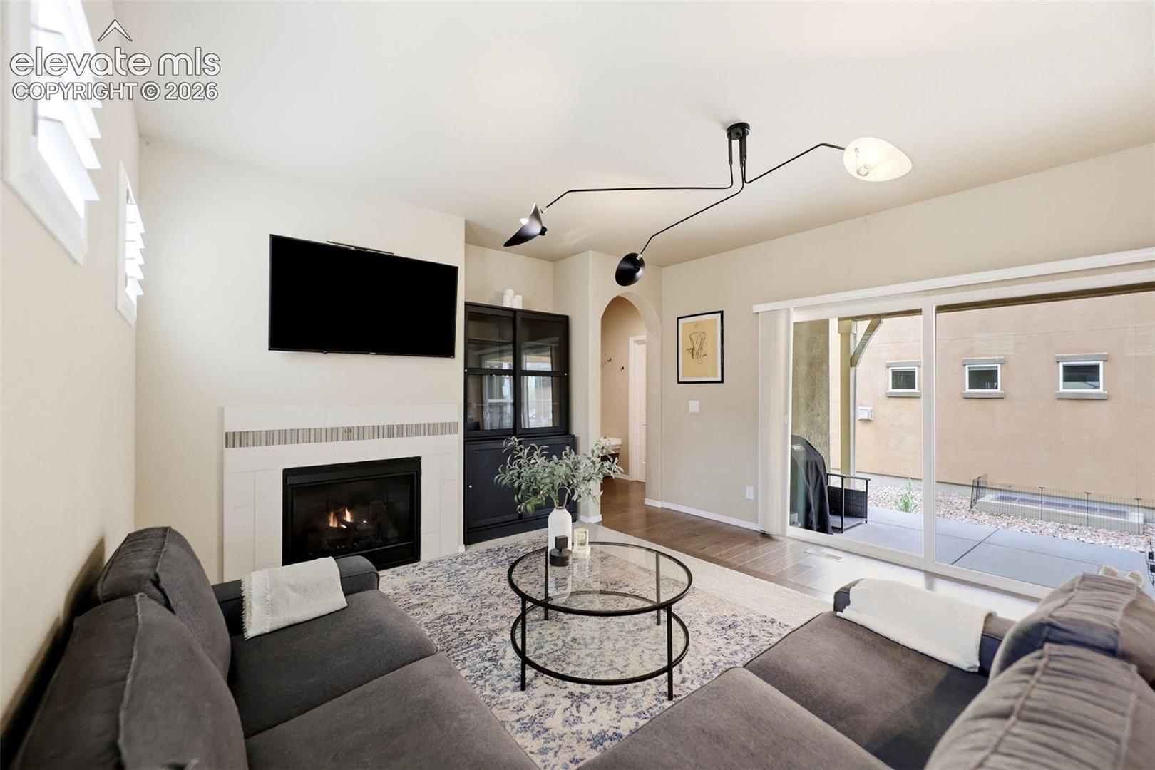Fireplace with tiled surround, ceiling-mounted multi-directional light fixture, cabinetry with glass panels, and sliding glass door