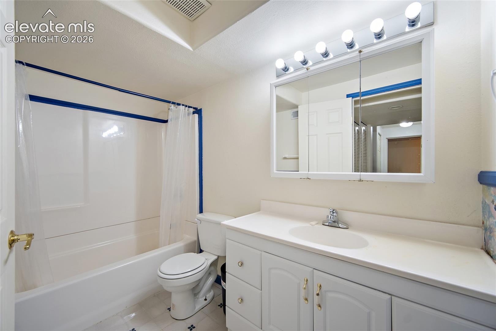 Bathroom featuring a white vanity with integrated sink, white cabinetry with gold-tone hardware, a mirrored medicine cabinet, and a five-bulb vanity light bar