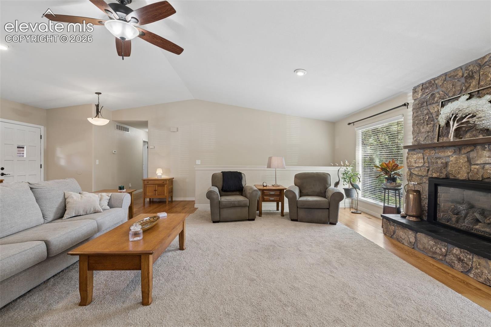 Vaulted ceilings, floor-to-ceiling natural stone fireplace with a black hearth, ceiling fan with integrated lighting