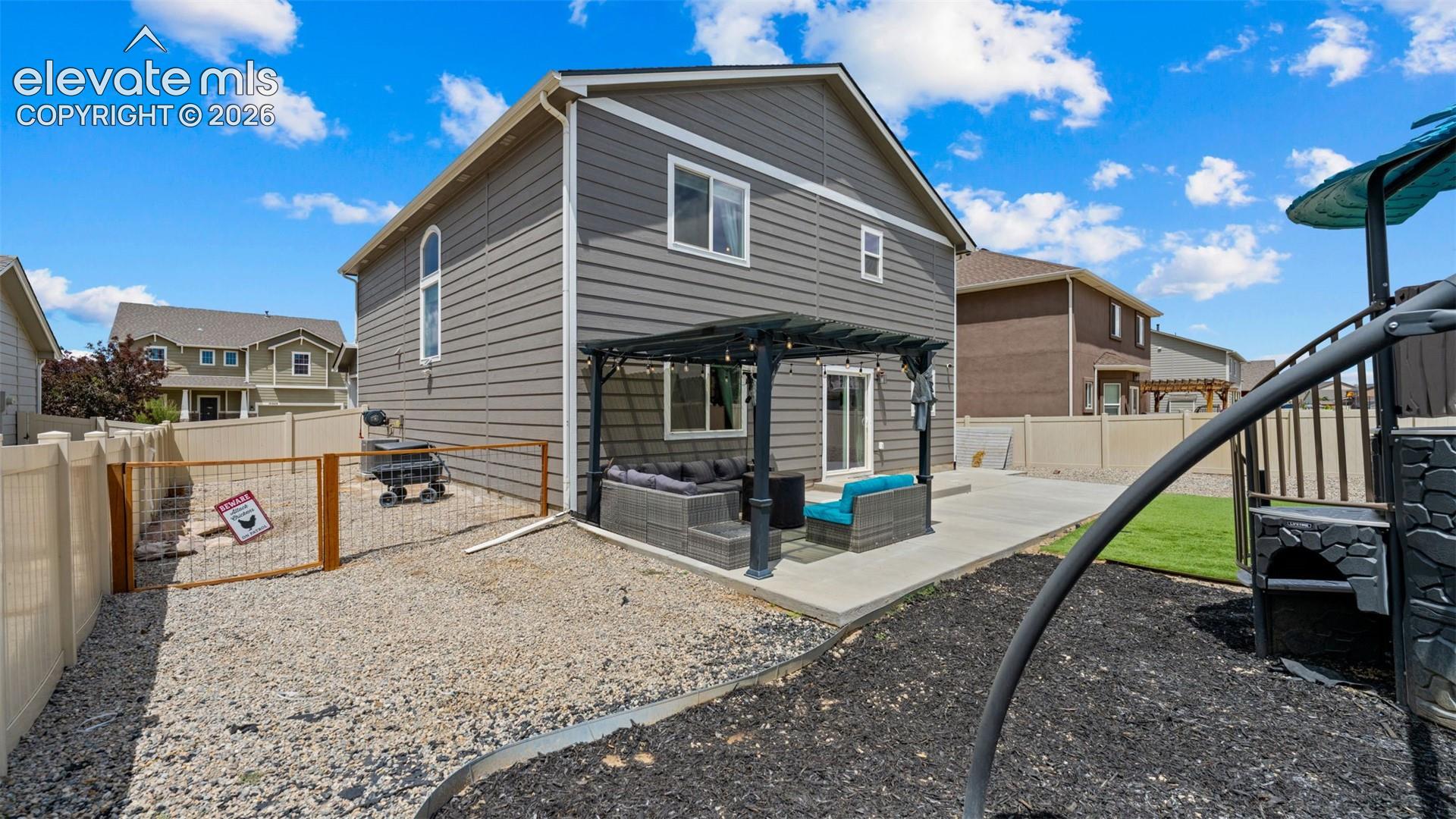 Rear exterior featuring gray horizontal siding, a concrete patio, a dark pergola, and an attached fenced gravel area