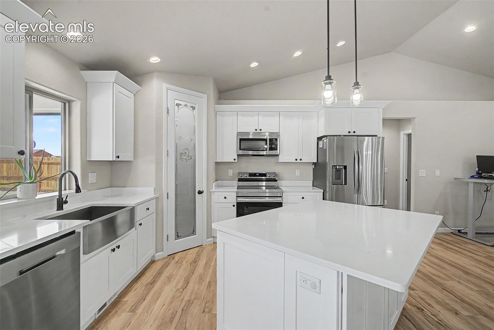 Bright kitchen featuring a substantial island with a white countertop, white cabinetry, stainless steel appliances, and wood-finish flooring
