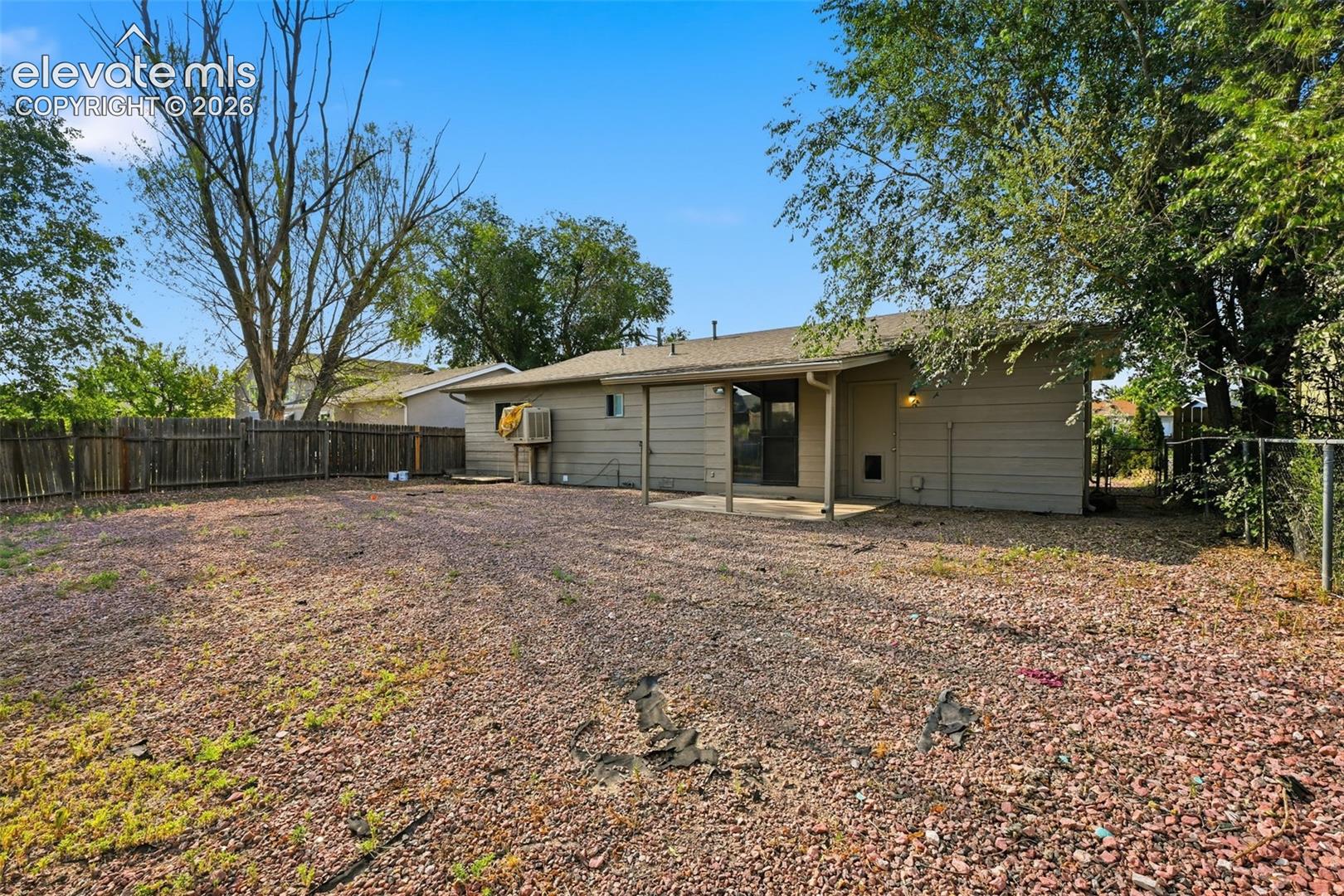 Expansive backyard featuring a gravel and sparse lawn surface, partial wood fence, and mature trees