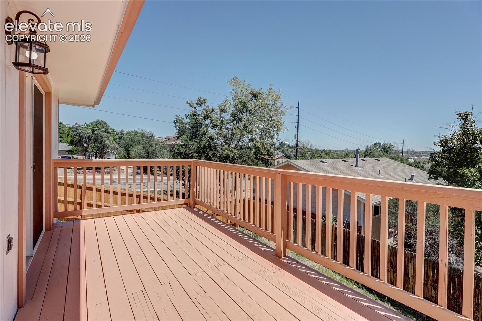 Elevated wooden deck featuring vertical baluster railings and an attached exterior wall-mounted lantern light