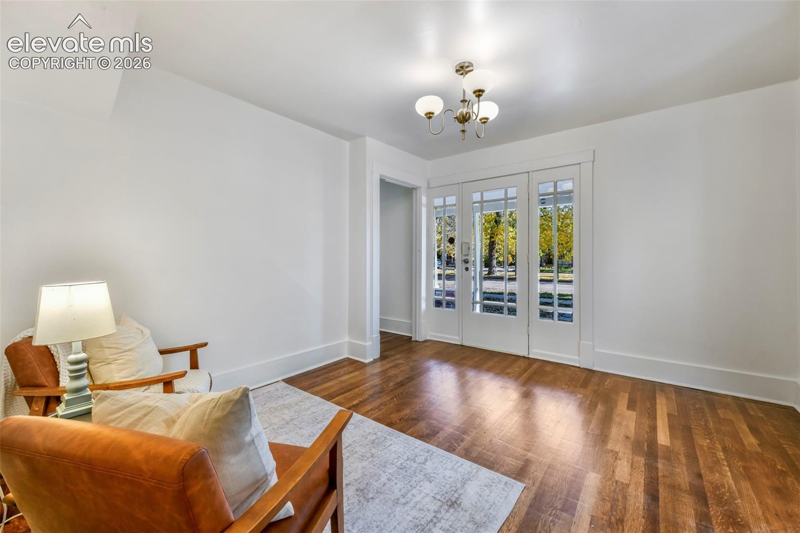 Interior space featuring wood-finish flooring, multi-pane glass entry door with matching side panels, and a traditional multi-arm chandelier