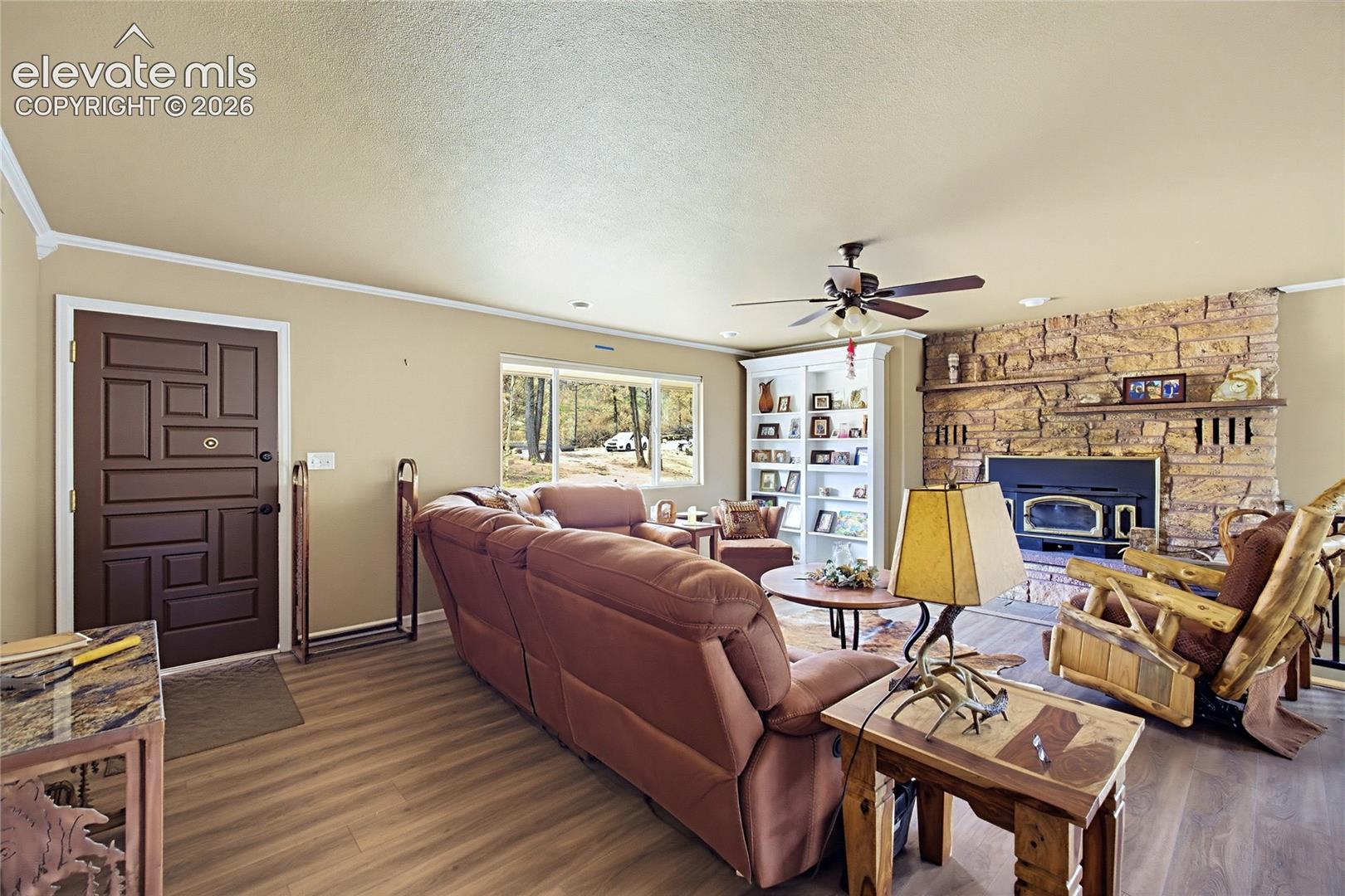 Living area featuring wood-finish flooring, a floor-to-ceiling stone fireplace with an integrated mantel, built-in shelving, and a dark-toned geometric paneled entry door