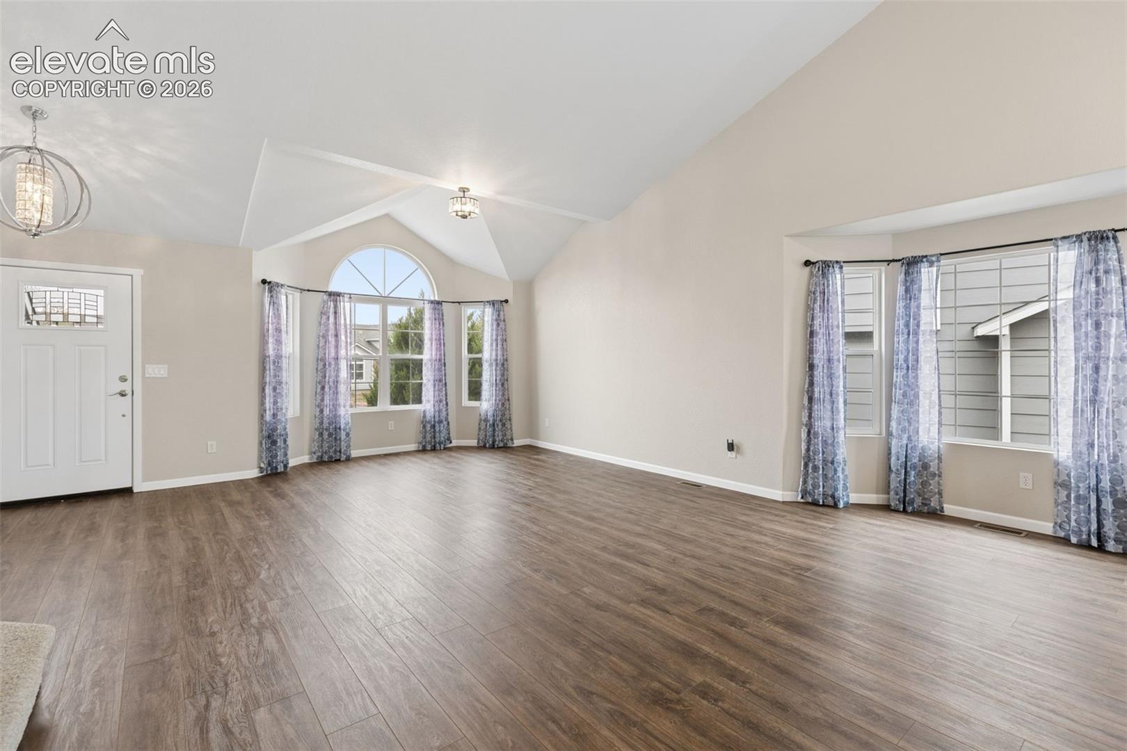 Vaulted ceilings, wood-finish flooring, bay windows, an arched window, and two tiered-style pendant light fixtures