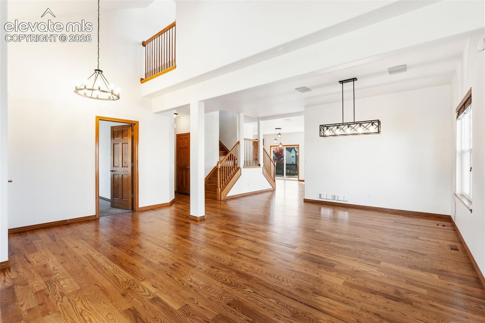 High-ceiling living area featuring wood-finish flooring, a tiered staircase with wood handrails, a geometric metal chandelier, and a wagon-wheel style light fixture