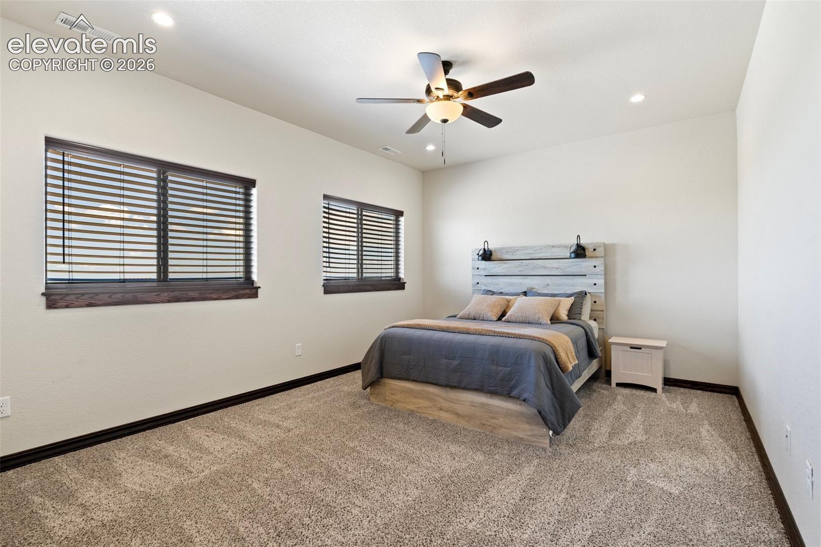 Carpeted room featuring two windows with dark wood trim, recessed lighting, and a ceiling fan