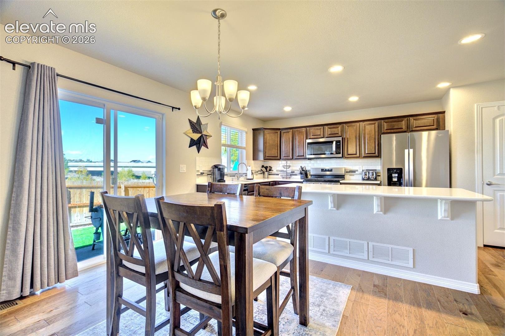 Kitchen featuring wood-finish cabinetry, stainless steel appliances, solid-surface breakfast bar, recessed lighting, and wood-finish flooring